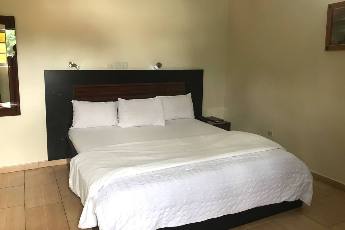 Una cama bien hecha con ropa blanca en una habitación con cabecera de madera y una mesita de noche pequeña.