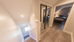 A modern loft-style bedroom with a large bed, a nightstand, and a window. - Ivory Lodge (Reading)