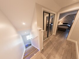 Egy modern, loft-stílusú hálószoba, amelyben egy nagy ágy, egy éjjeliszekrény és egy ablak található.