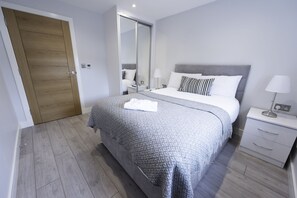 A modern bedroom with a large bed, a nightstand, a mirror, and a wooden door.