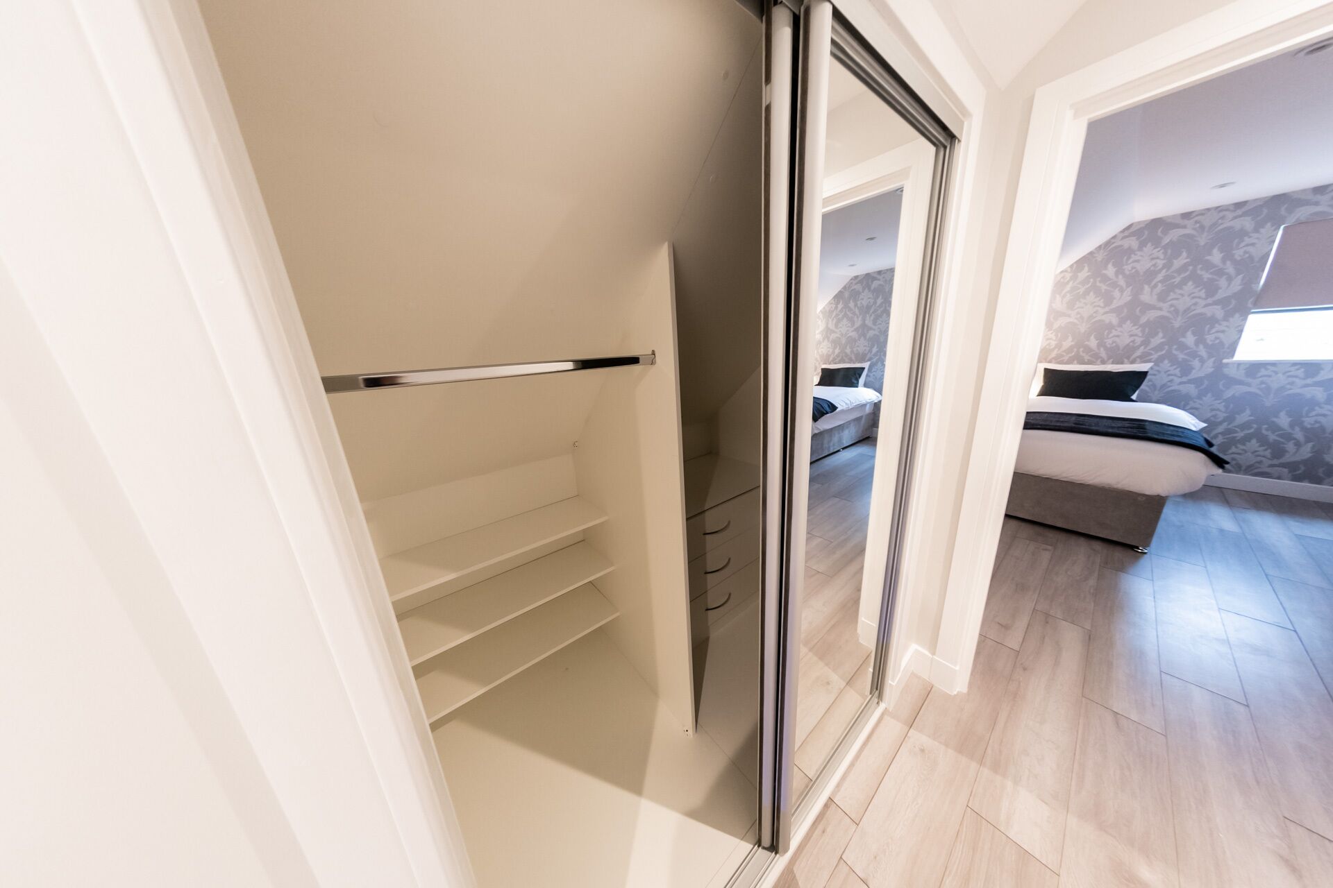A modern bedroom with a large bed, a built-in wardrobe, and a sliding glass door leading to another room.