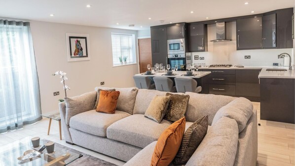 A modern living room with a grey sofa, a glass coffee table, and a dining area with a table set for four.