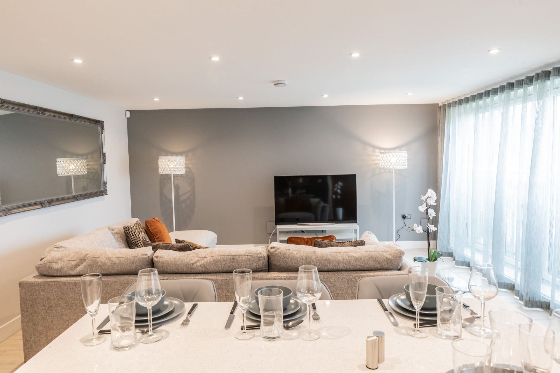A modern living room with a sectional sofa, a flat-screen TV, and a dining area set for six.
