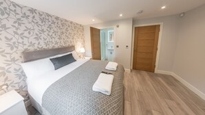 A bedroom with a bed, bedside table, and a nightstand. There is a door leading to another room. - Ivory Lodge (Reading)