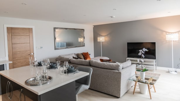 A modern living room with a grey sofa, a dining table with chairs, a flat-screen TV, and two floor lamps. - Ivory Lodge (Reading)