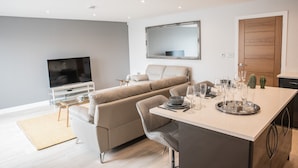 A modern living room with a sofa, TV, and dining area with a tray of glasses. - Ivory Lodge (Reading)