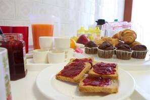 Une table de petit-déjeuner avec des tartines, des muffins, des croissants et un saladier de fruits.