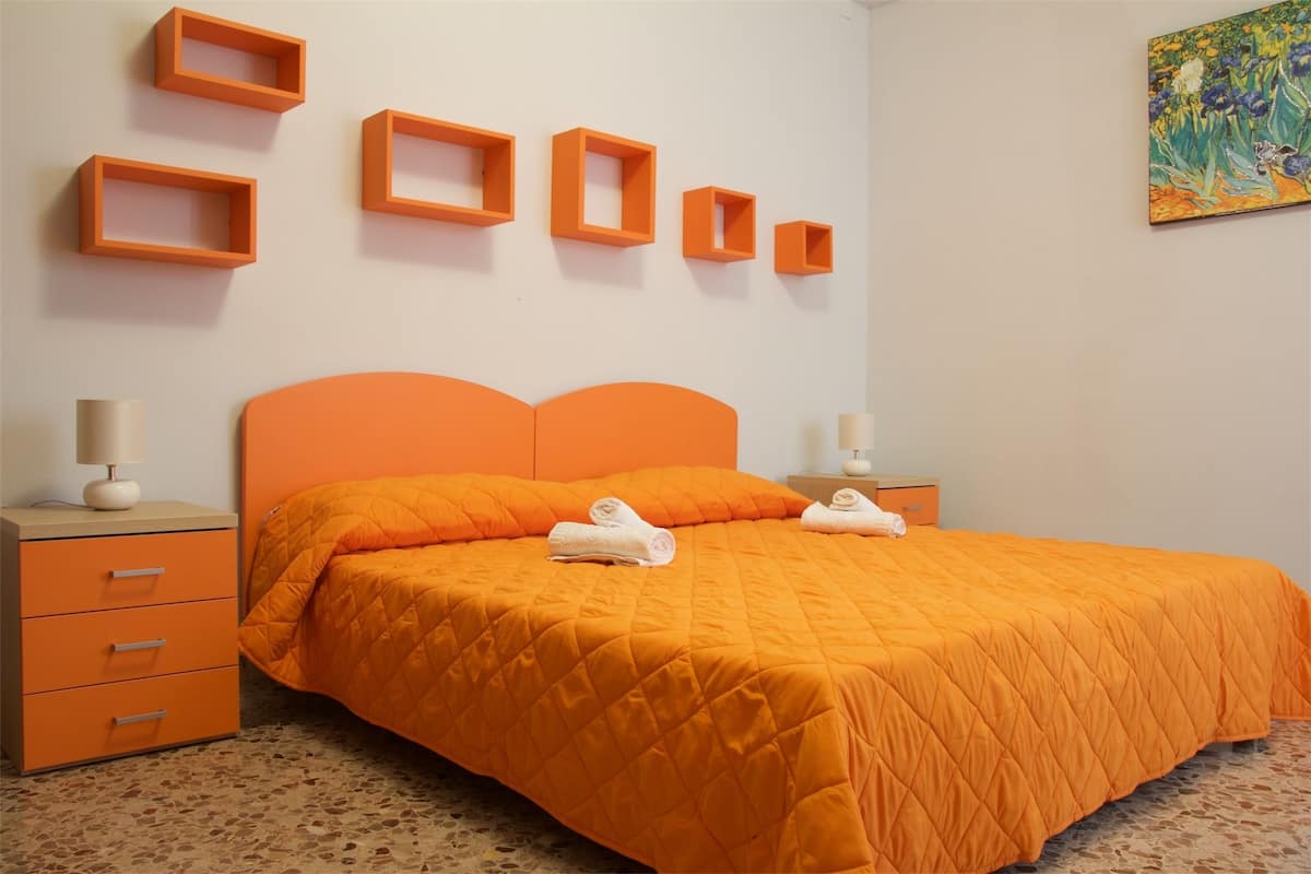 Een slaapkamer met een oranje sprei, bijpassende nachtkastjes en een aantal oranje wandplanken.