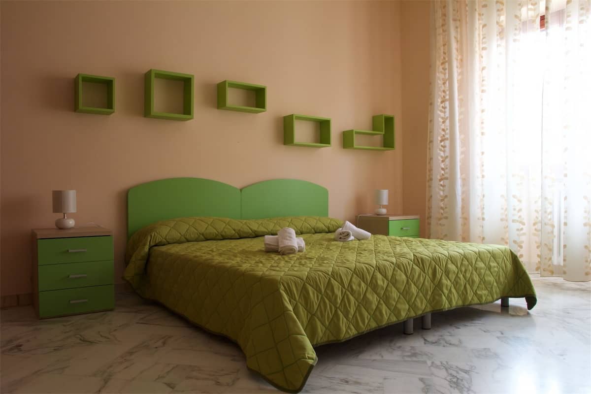 Een slaapkamer met een groen bed, een groen nachtkastje en een groene dressoir. Er hangen vier groene vierkante lijstjes aan de muur.