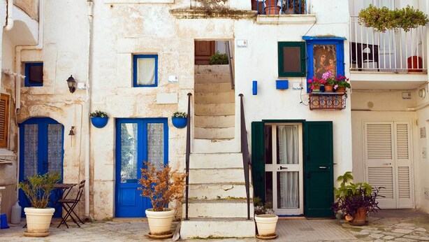 Eine enge Straße mit Gebäuden, die blaue Türen und Fenster, eine Treppe und Blumentöpfe zeigen.