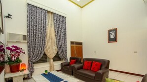 A living room with a brown sofa, two red cushions, a potted plant, and a small table with a lamp. - Meiden (Wujie)