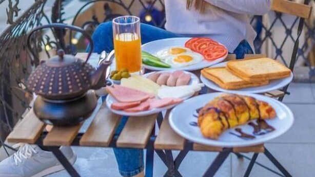 A person sitting at an outdoor table with a meal consisting of eggs, tomatoes, toast, and a croissant. - Sahil Inn Hotel (Baku)