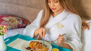 A person sitting on a bed with a tray containing food and drinks. - Sahil Inn Hotel (Baku)