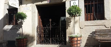 A building entrance with a wrought iron gate, potted plants, and a bench.
