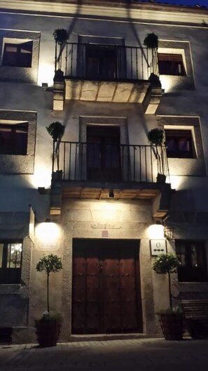 A building with a central entrance, multiple windows, and balconies with plants. - Casa Rural con encanto Los Postigos (Banos de Montemayor)