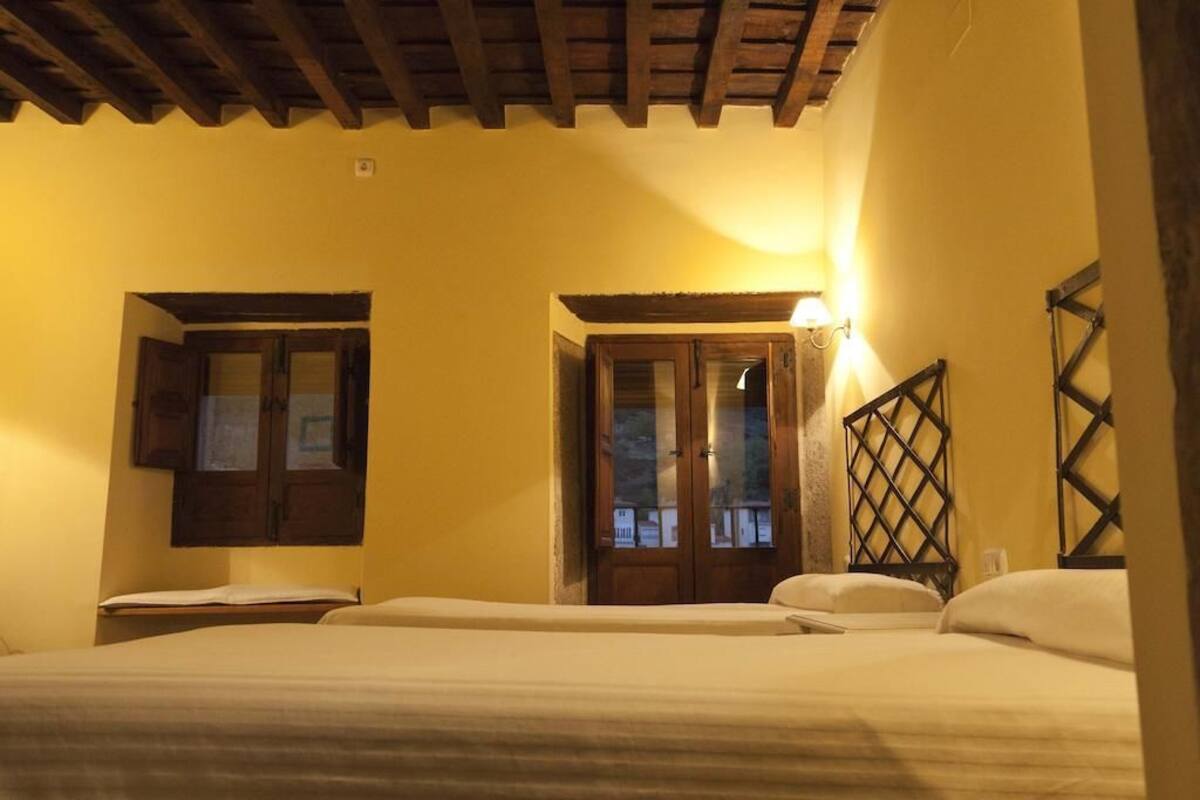 A room with two beds, wooden beams on the ceiling, and a window with a wooden shutter.