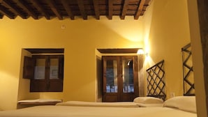 A room with two beds, wooden beams on the ceiling, and a window with a wooden shutter.