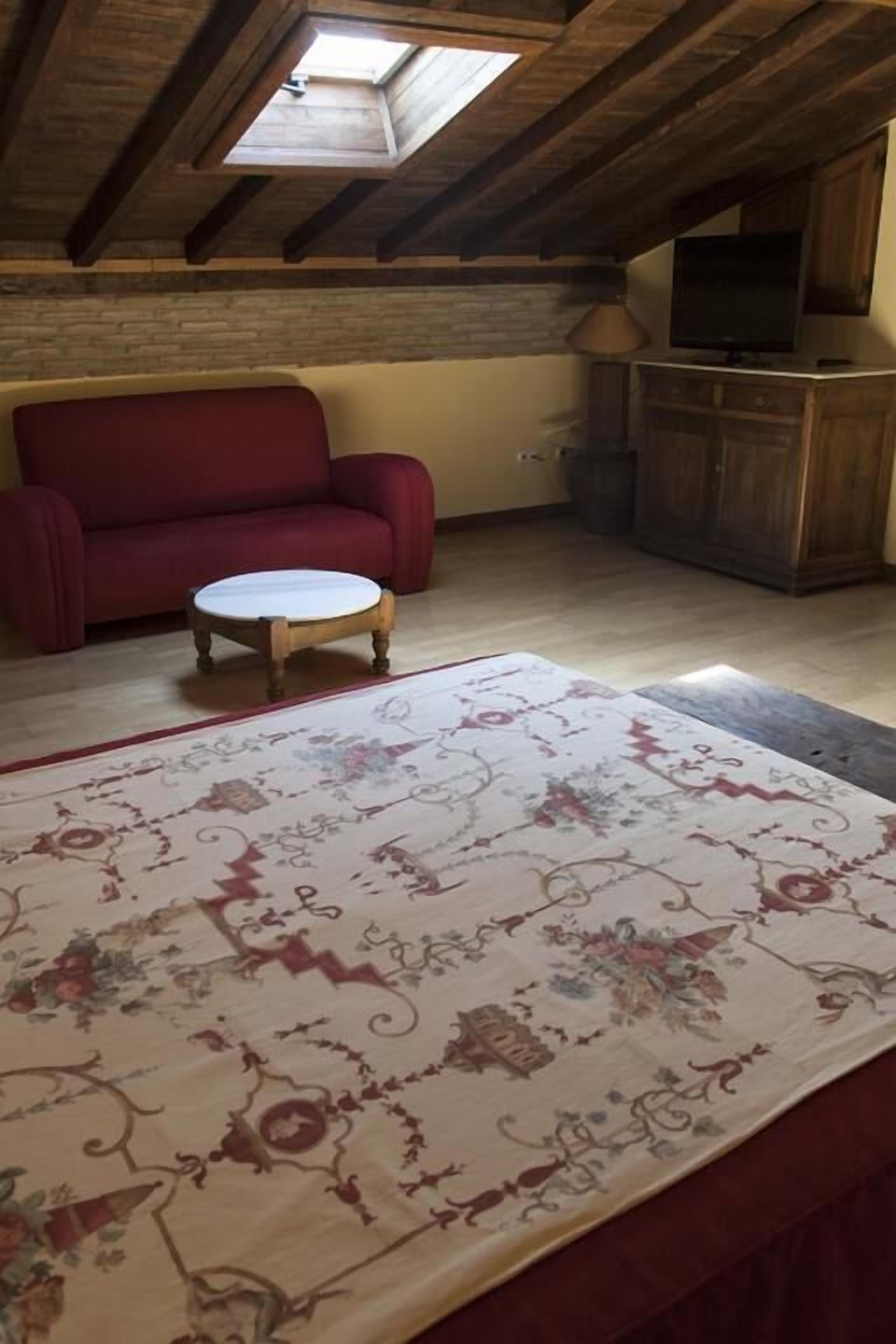 A room with a red sofa, a small round table, a patterned rug, and a wooden ceiling with a skylight.