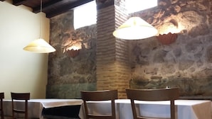 A dining area with stone walls, wooden chairs, and hanging lamps.