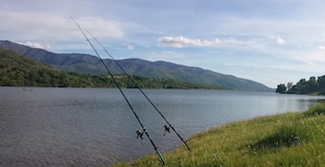 Une canne à pêche est installée au bord d’un lac, avec des montagnes en arrière-plan.