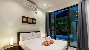 A hotel room with a bed, a nightstand, an air conditioner, a painting, and a view of a pool through a glass door. - Modern 3BR Pool Villa by Intira Villas (Rawai)