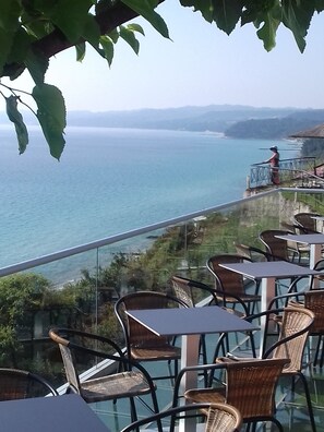 A terrace with wicker chairs and tables overlooking a coastal view. - Aegean Blue Studios (Kassandra)