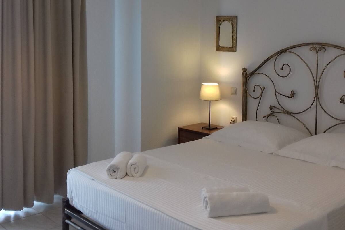 A neatly made bed with white linens and towels, a bedside lamp, and a metal headboard.