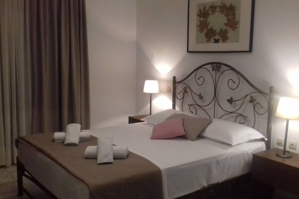 A neatly made bed with pillows and a blanket, two bedside lamps, and a framed leaf artwork on the wall.