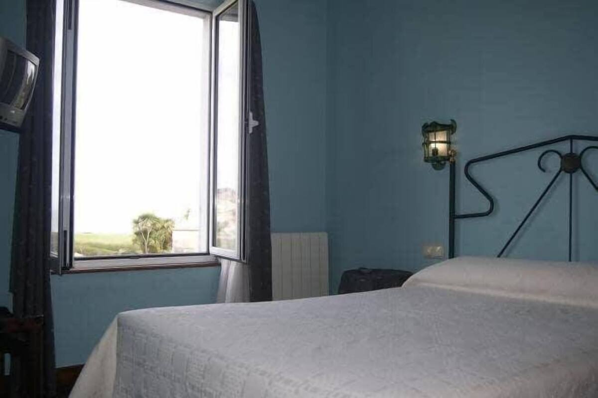 A bedroom with a bed, a window with curtains, a wall-mounted lamp, and a radiator.
