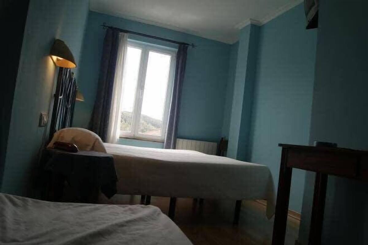 A room with two beds, a window with curtains, a lamp, and a small table.