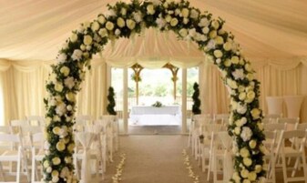 Um corredor de casamento com cadeiras brancas e um arco floral.