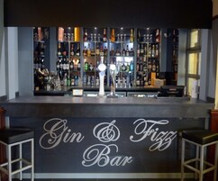 Um bar com uma placa indicando "Gin & Fizz Bar" e prateleiras repletas de garrafas diversas.
