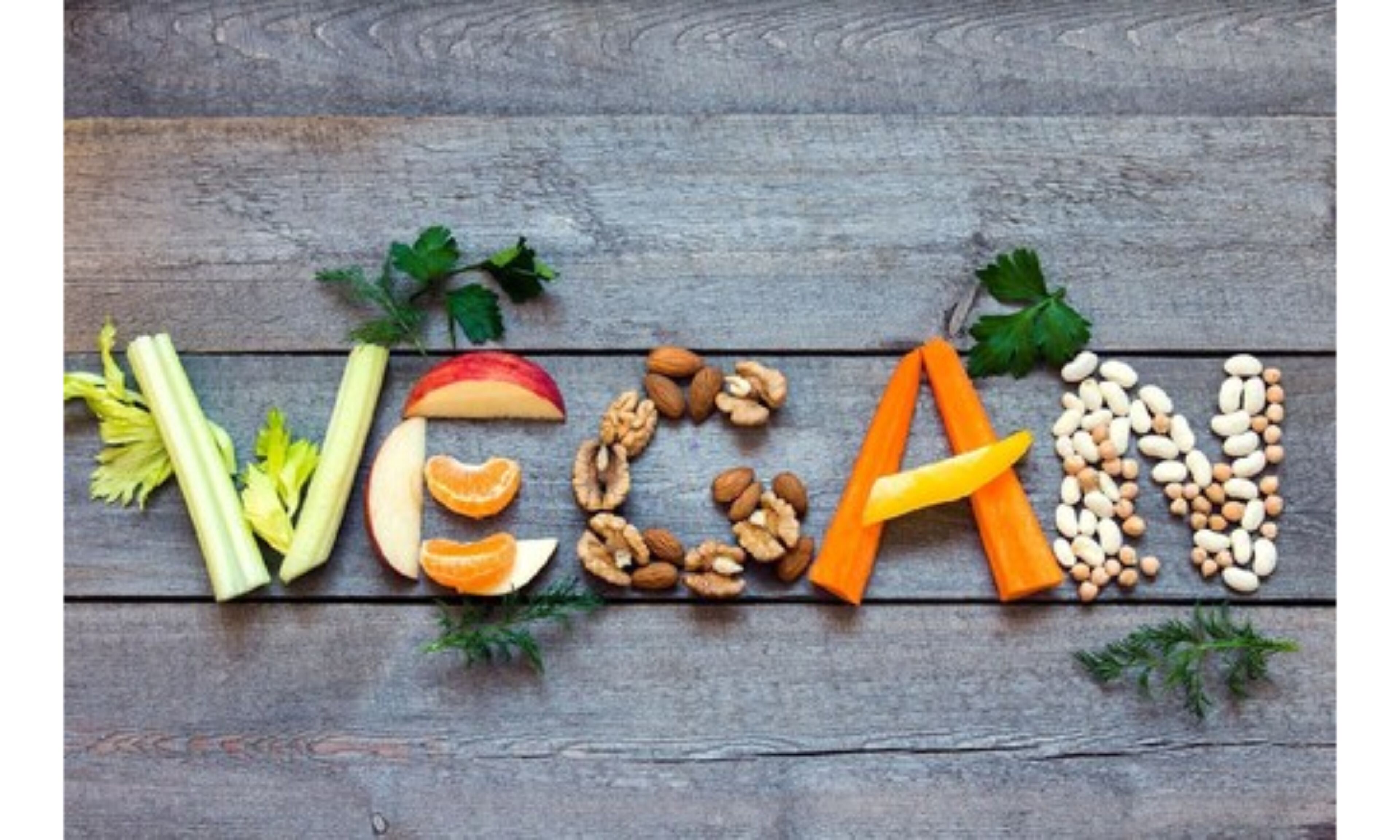 Une surface en bois sur laquelle le mot « VÉGAN » est écrit à l’aide de différents légumes et légumineuses.