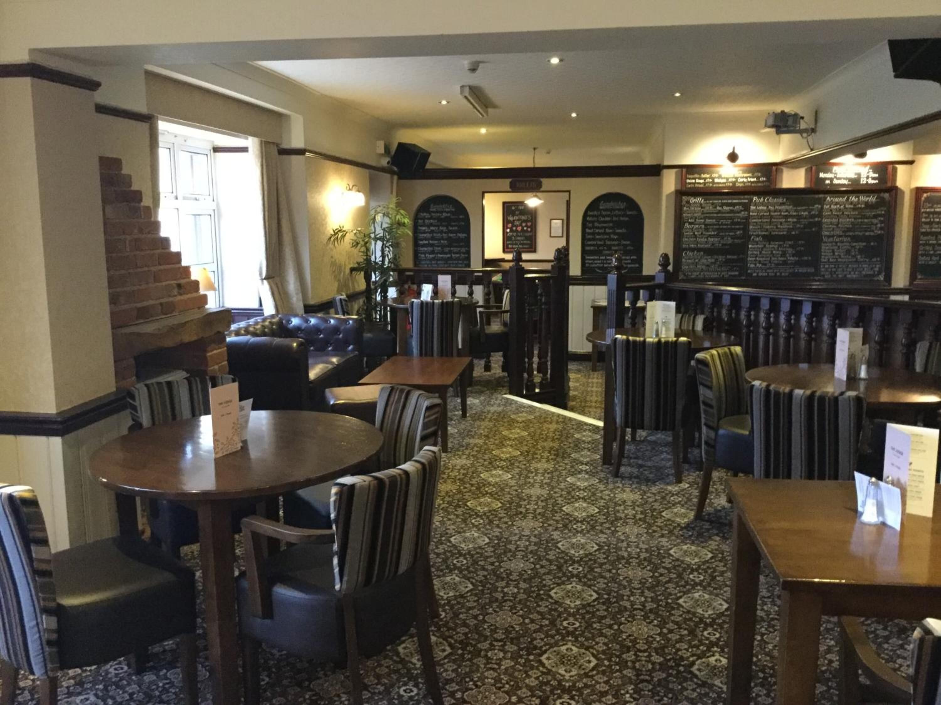 Een restaurant interieur met ronde tafels, gestreepte stoelen, een kamerbreed tapijt en een trap.