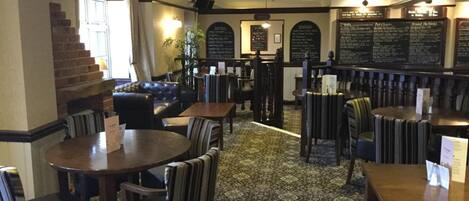 Een restaurant interieur met ronde tafels, gestreepte stoelen, een kamerbreed tapijt en een trap.