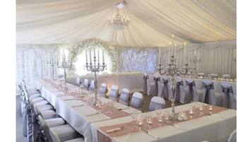 Un espace événementiel aménagé sous une tente, avec des tables dressées pour une occasion formelle, agrémenté de lustres et de compositions florales.