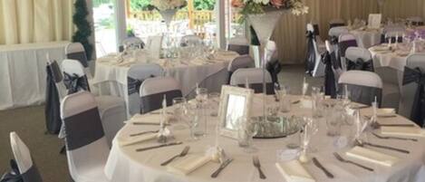 A banquet hall with round tables set for a formal event, featuring white tablecloths and black chair sashes.