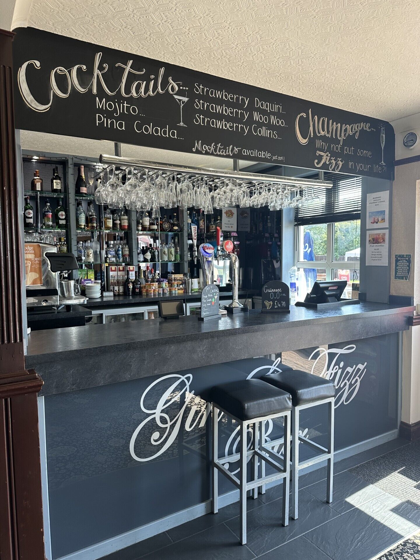 Een bar met een krijtbord waarop cocktails staan vermeld en een bord dat champagne promoot.