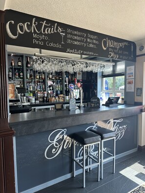Zona de bar con un menú en pizarra que enumera cócteles y un cartel que anuncia champán.