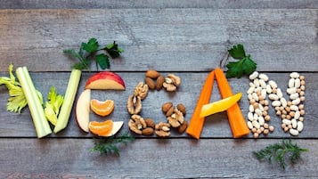 A wooden surface with the word "VEGAN" spelled out using various vegetables and legumes.