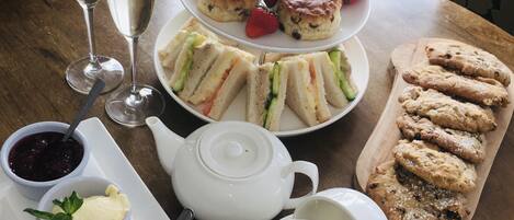 A three-tiered dessert plate with scones and strawberries, a tray of scones, sandwiches, and cookies, a teapot, cups, and bowls of cream and jam.
