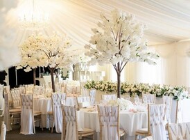 Uma sala de banquetes com mesas redondas, cadeiras com toalhas brancas e arranjos florais.
