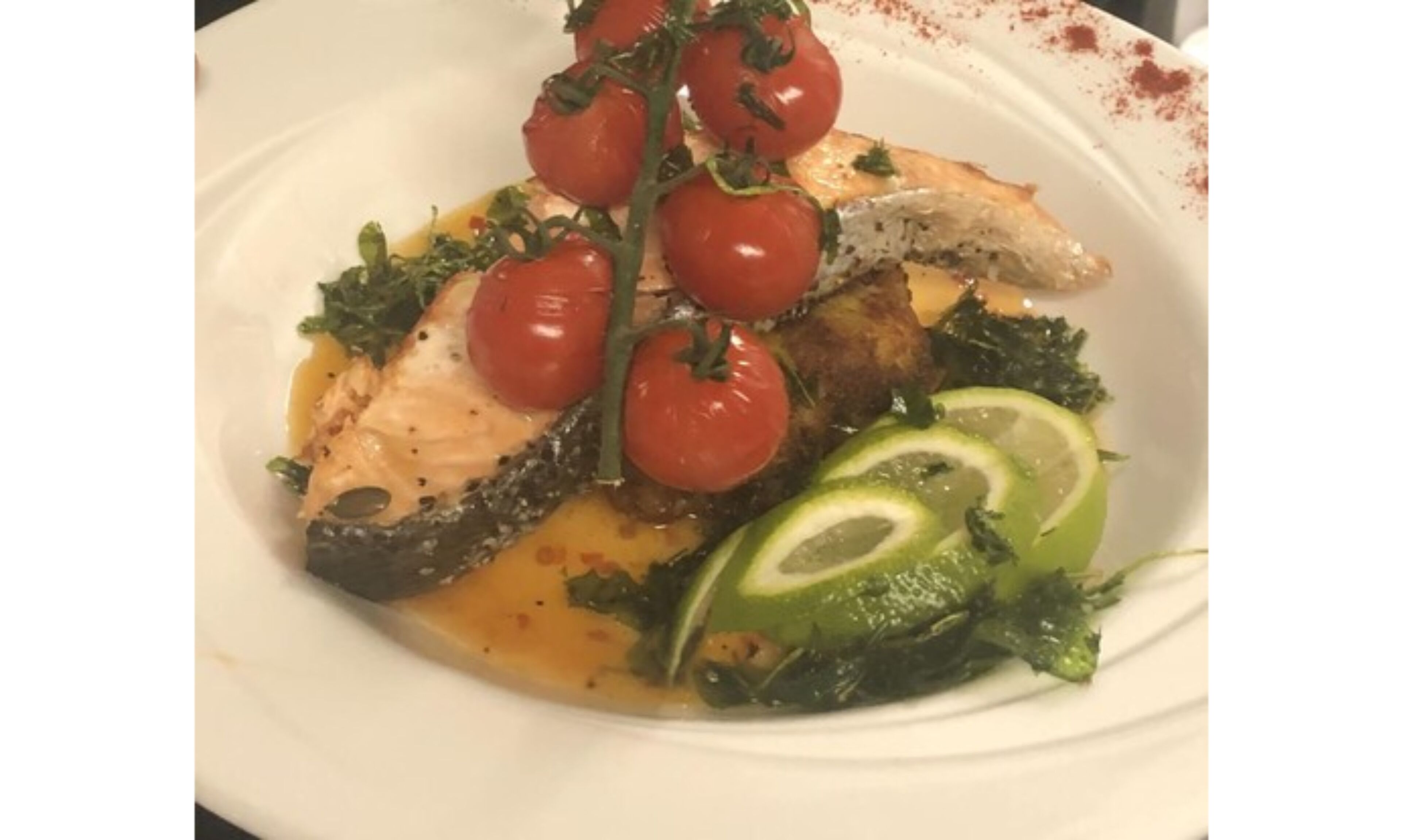 A plate of food with fish, cherry tomatoes, and greens.