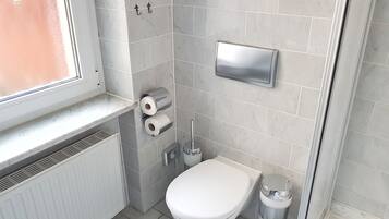 A small bathroom with a toilet, a trash can, and a toilet paper holder.