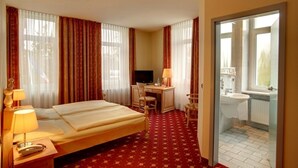A hotel room with a bed, desk, chair, TV, lamp, and a bathroom visible through an open door. - Hotel Kronprinz (Minden)