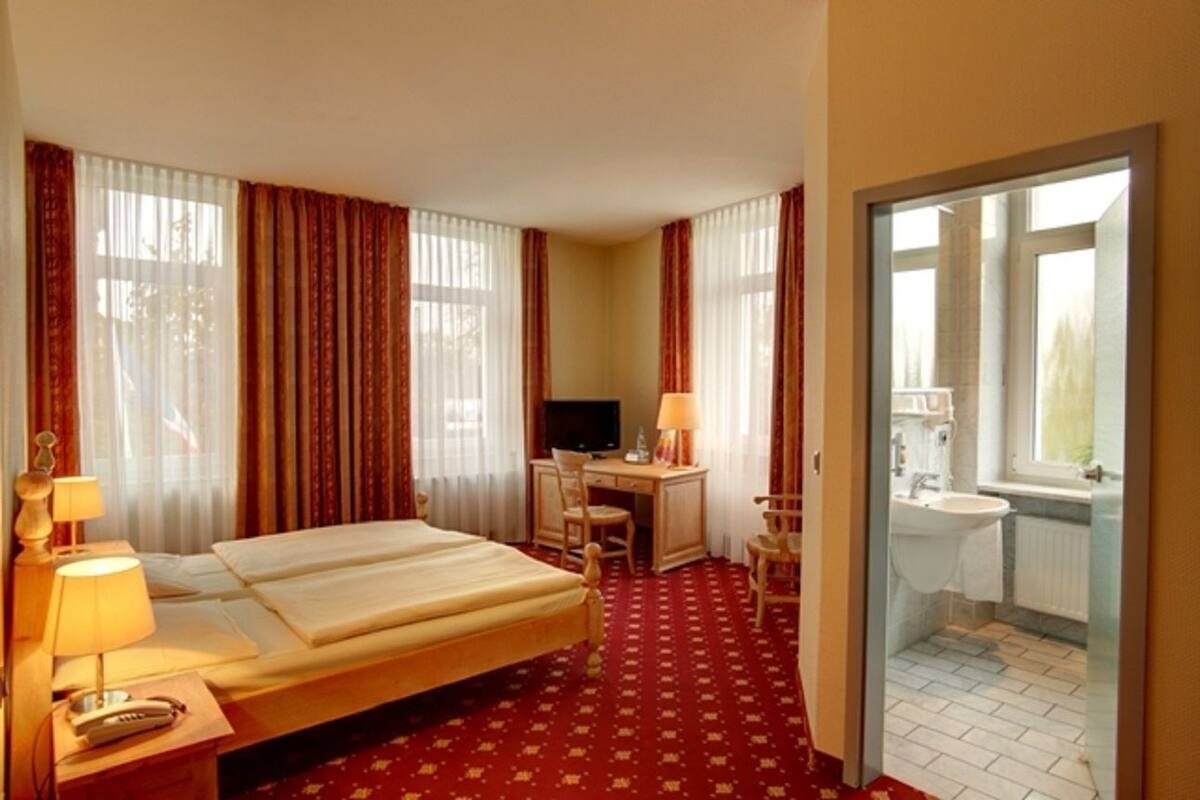 A hotel room with a bed, desk, chair, TV, lamp, and a bathroom visible through an open door.