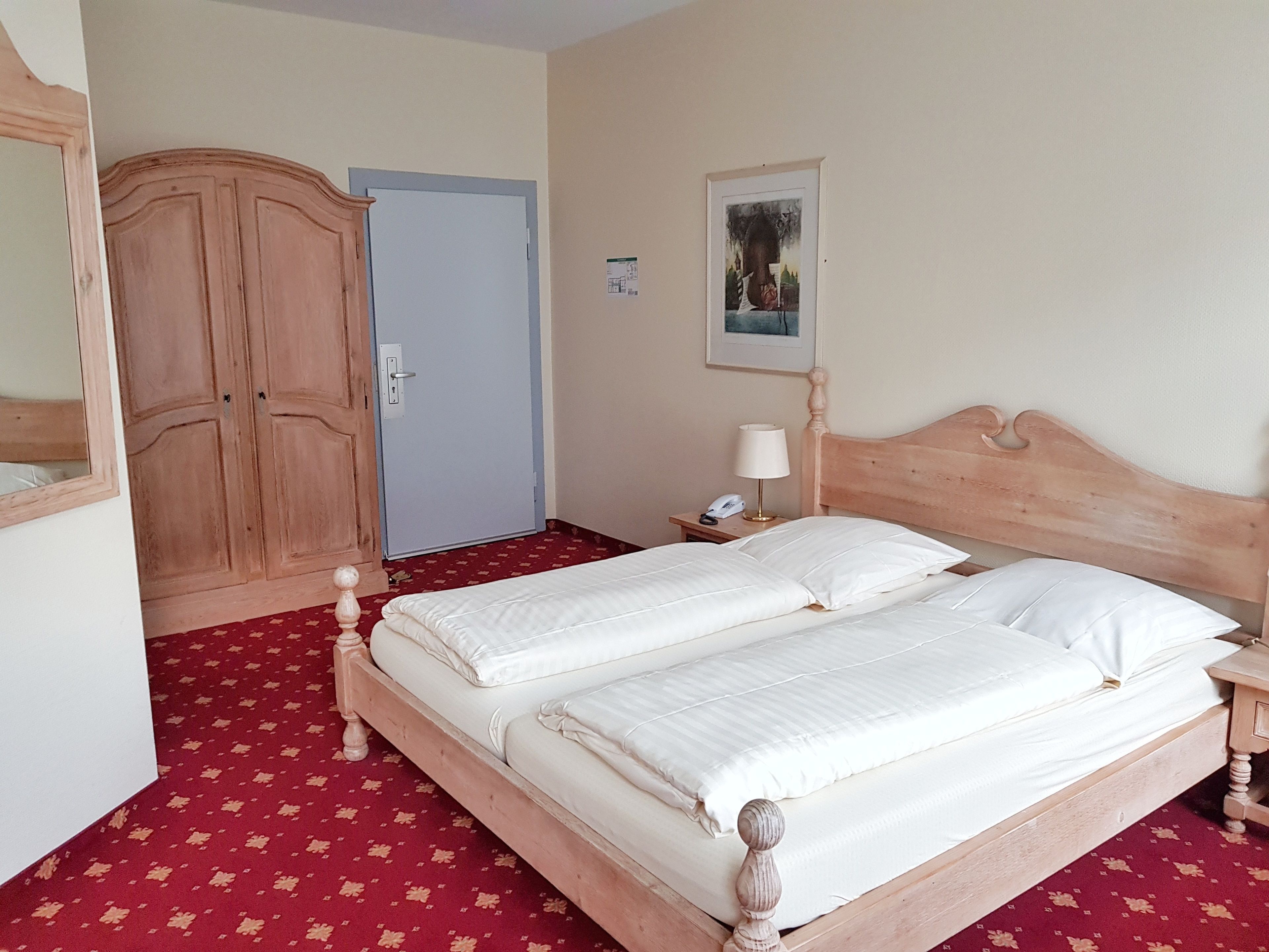 Une chambre avec un lit double, une armoire en bois, une table de chevet avec une lampe et une porte.