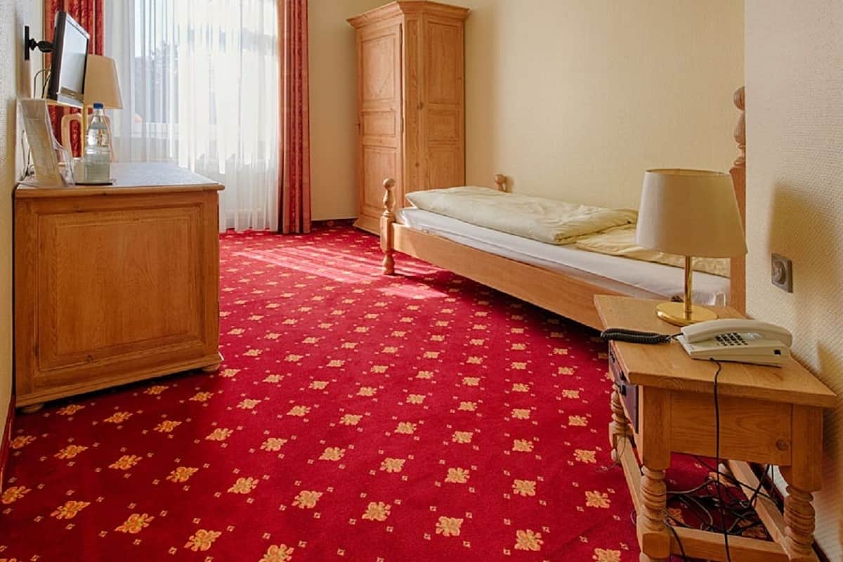 A hotel room with a single bed, a wooden wardrobe, a desk with a lamp, and a telephone.