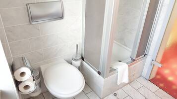 A bathroom with a toilet, two rolls of toilet paper, a towel rack, and a shower area.