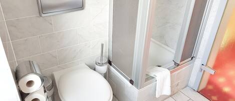 A bathroom with a toilet, two rolls of toilet paper, a towel rack, and a shower area.